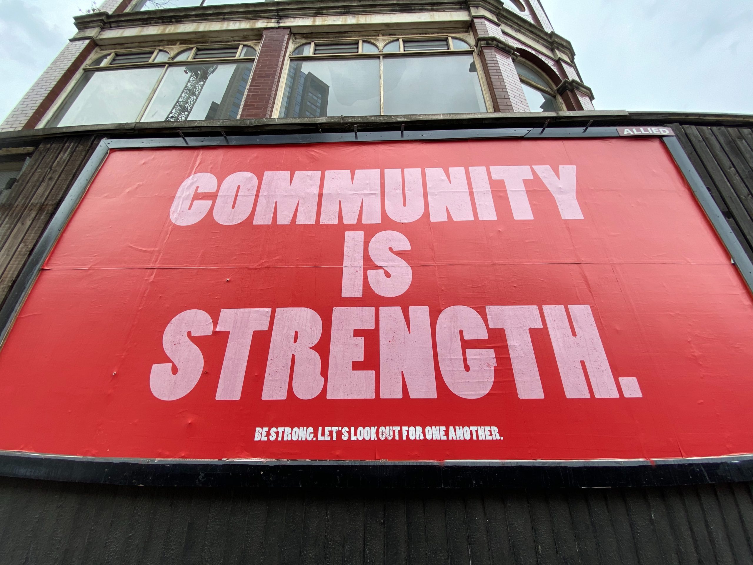 Red billboard with "Community is strength." written on in in pink.